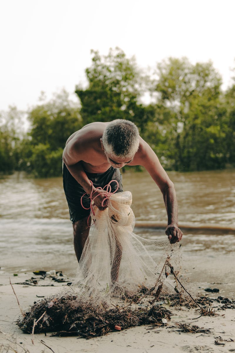 A man skillfully handles a fishing net along a riverbank in Banting, Malaysia.